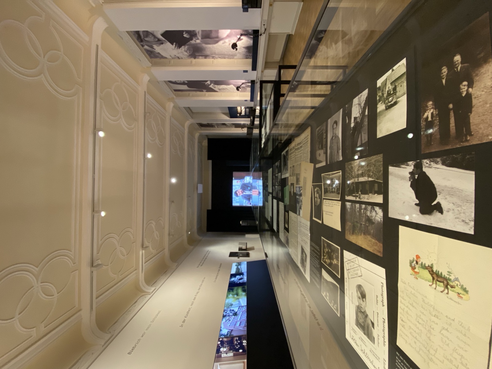 Blick durch den Saal über die Vitrinen hinweg auf eine Projektion am anderen Ende