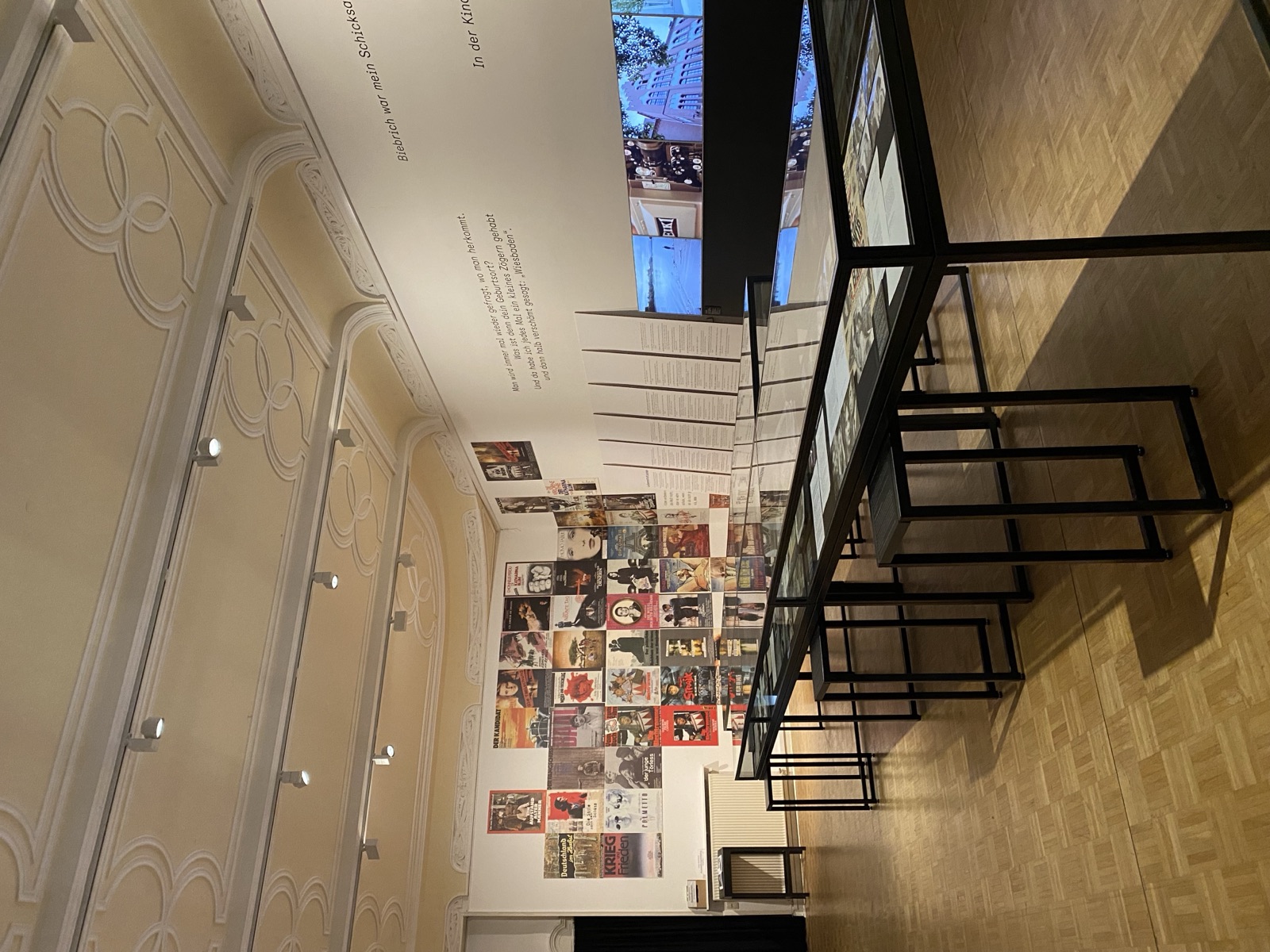 Saal mit einer Wand aus Filmplakaten, Vitrinen und einem Bildschirm an der rechten Wand